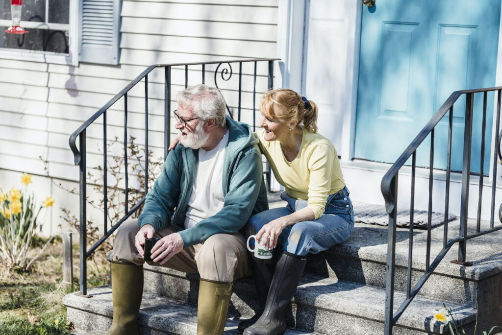 Older couple sitting on front porch in the spring in front of their clean home