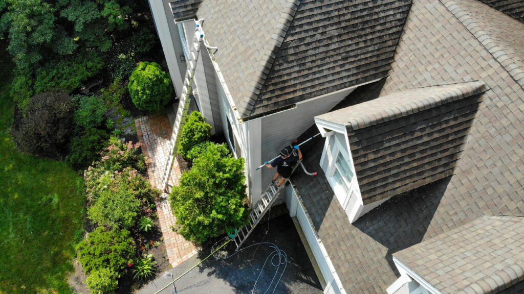 Aerial shot of residential home with ladders while CleanME exterior owner power washes roof